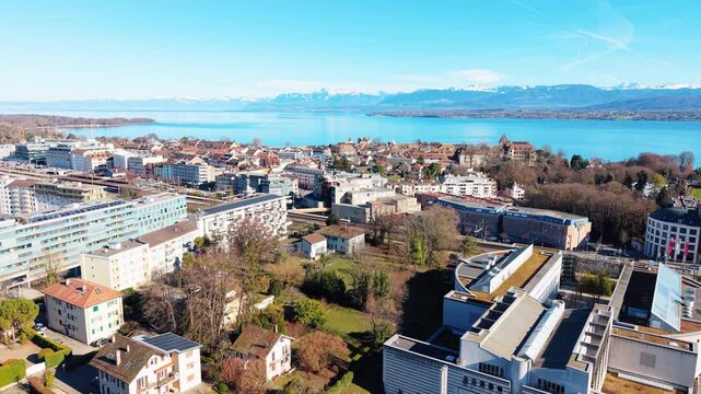 Aerial: Nyon cityscape during the day with Lake Geneva and mountains in Canton of Vaud, Switzerland, pull out drone shot