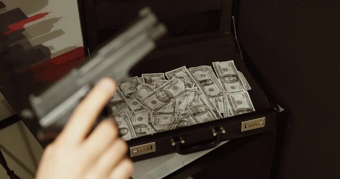 a handgun in front of an open briefcase filled with cash. Concept of robbery, organized crime, extortion, illegal money, and criminal activity.