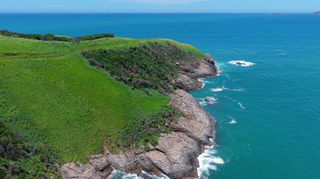 Aerial ascend over green coastal hills and rocky shoreline meeting blue Atlantic Ocean in Buzios Brazil