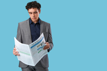 Handsome young man in stylish suit reading newspaper on blue background