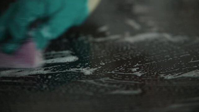A person uses a sponge with cleaning modern induction electric stove, focusing on the movement and application of product.