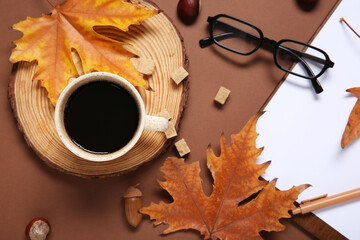 Cup of coffee with clipboard, eyeglasses, autumn leaves, acorn and chestnuts on brown background © Pixel-Shot