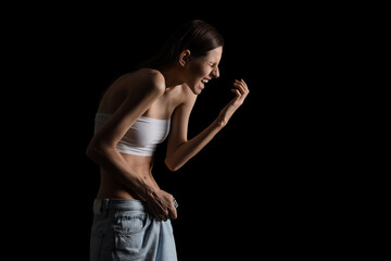Naklejka premium Young woman with anorexia in loose jeans screaming on black background