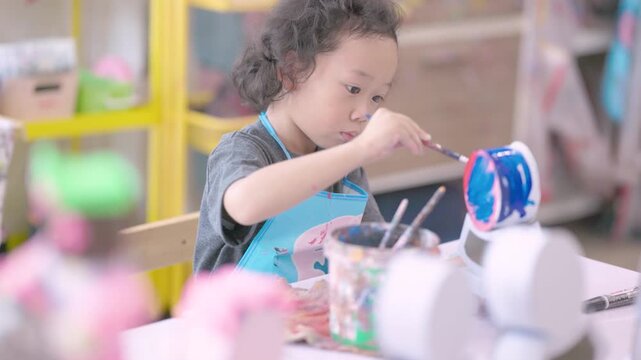 Young child learning painting while decorating a plaster figurine with a brush, developing artistic skills, creativity, concentration, imagination.