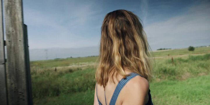 Woman looking out over a countryside field from a fence