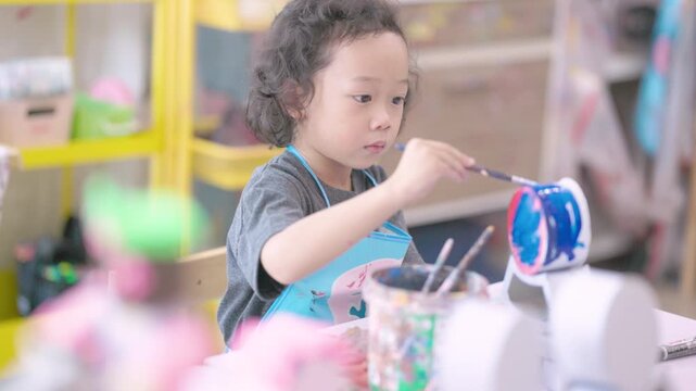 Young child learning painting while decorating a plaster figurine with a brush, developing artistic skills, creativity, concentration, imagination.