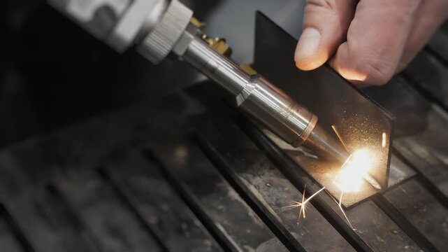 Industrial laser welding of metal parts with filler wire producing bright sparks during precision metal fabrication process in manufacturing environment.
