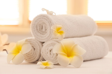 White towels and plumeria flowers on couch in spa salon, closeup