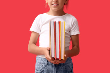 Fototapeta premium Cute little girl holding books on red background