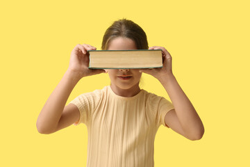 Fototapeta premium Cute little girl holding book on yellow background