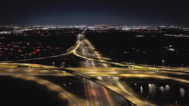 An aerial timelapse of a large stack interchange on Florida's Turnpike on a clear night. The camera truck right, pan left and boom down over the highway intersection and rain water retention ponds.