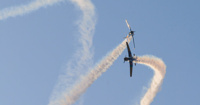 Two aircraft performing aerobatic maneuvers with smoke trails against a clear sky during an aerial aviation display