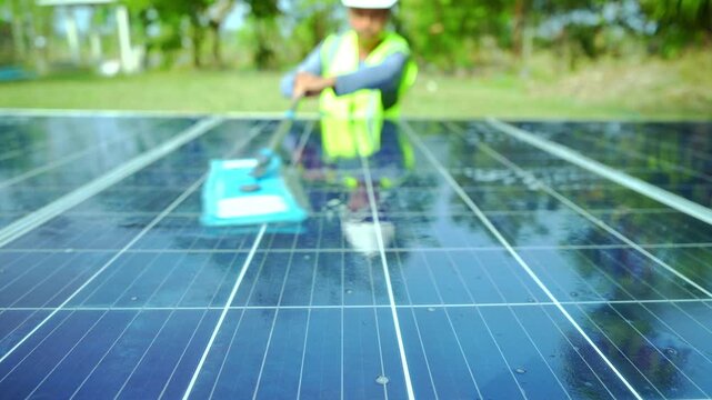 Alternative power plant worker in uniform cleaning solar panels with mop.