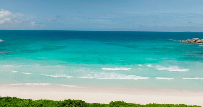Crystal clear azure waves gently touching the pristine white sandy shore with lush greenery nearby. Anse Cocos. Seychelles, La Digue.