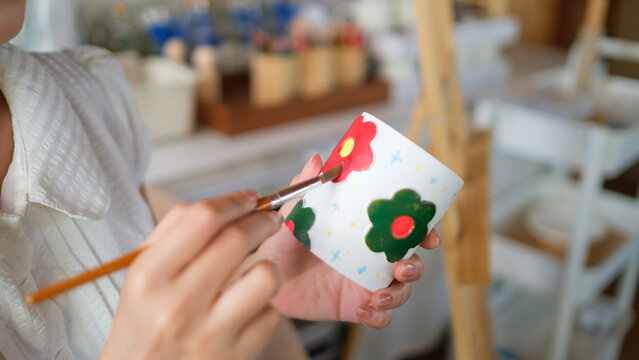 Close up of an artist painting flowers on a handmade mug in a workshop, handmade art and craftsmanship.