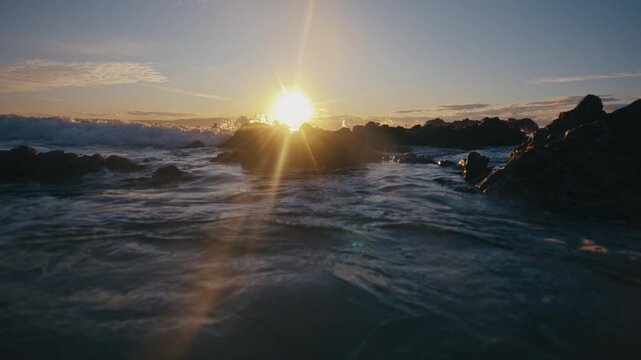 Backlit wave crests as sunlight flares by moving water near rocky shore