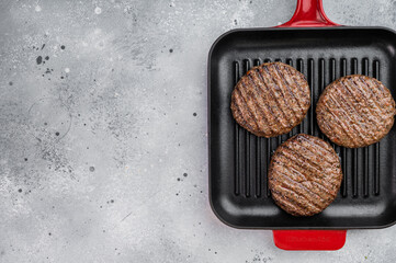 Grilled beef and lamb burger patties with seared crust in cast iron grill pan. Cooked juicy meat on light stone background with copy space. © Mironov