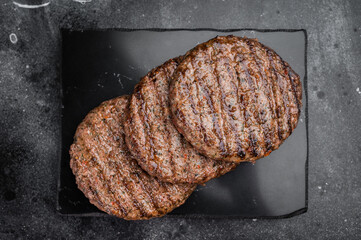 Grilled beef and lamb patties with seared crust on black slate plate. Cooked juicy meat on dark stone background with copy space. © Mironov