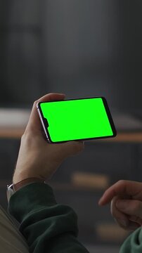 Person holding smartphone with bright green chroma key screen in horizontal orientation, ready for video playback, streaming content, app display or digital interface mockup