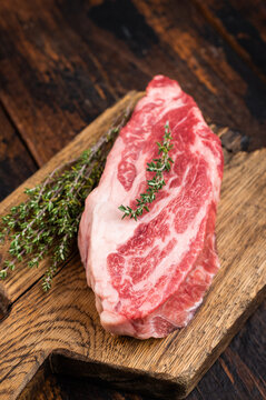 Raw beef chuck eye roll steak on wooden board with thyme and pepper. Marbled beef cut on dark wood background top view copy space.
