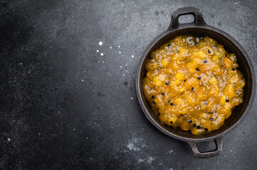 Fototapeta premium Mango and passion fruit sauce in cast iron pan on dark background, gourmet tropical fruit reduction with glossy texture