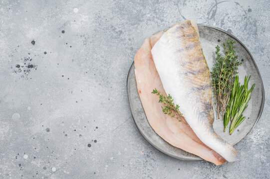 Raw pike perch fillets with skin and fresh herbs on light background, lean freshwater white fish for healthy cooking.