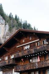 Obraz premium Scenic alpine village with traditional houses and green pastures set against dramatic mountains and rocky cliffs in a peaceful rural landscape.