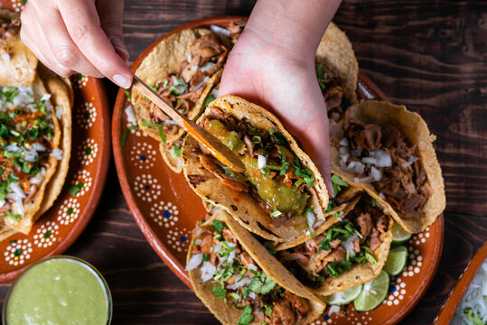 Close-up of tacos al pastor, prepared with fresh ingredients and green sauce on a wooden background.