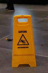 A yellow plastic warning sign on the floor with a German slippery caution message. The image represents safety, risk prevention, and public awareness.