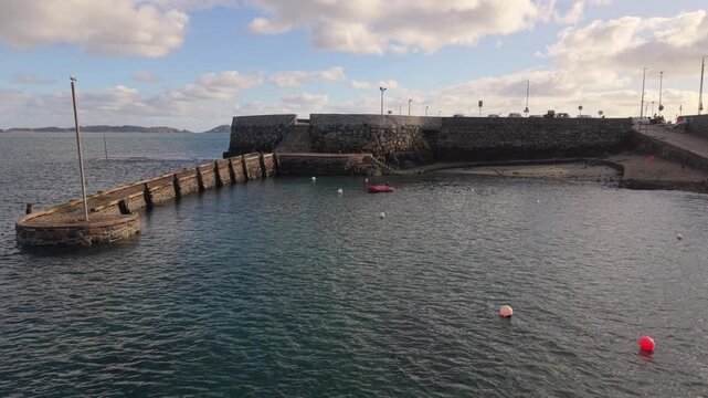 Salerie Corner St Peter Port Guernsey stationery drone footage of water gently coming into ancient harbour at mid tide with small boat at anchor in shaded sun with calm water and views across to Herm