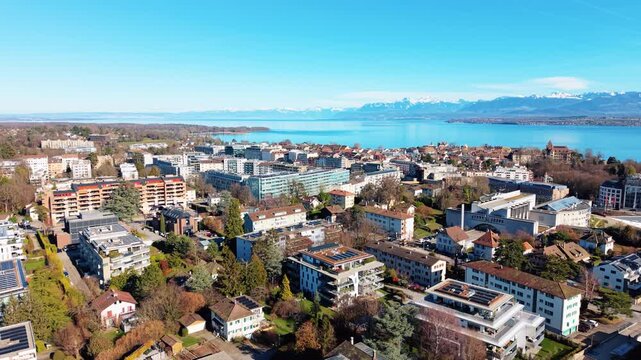 Aerial: Nyon cityscape during the day with Lake Geneva in Canton of Vaud, Switzerland, jib up drone shot