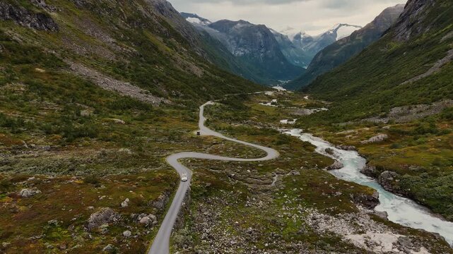 White modern camping van driving through dramatic Norway valley with river and green tundra. Aerial