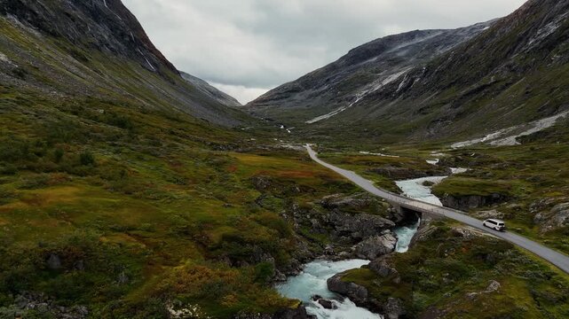 Modern camping van on empty mountain road crossing a bridge across a glacial river in Norway highlands. Aerial