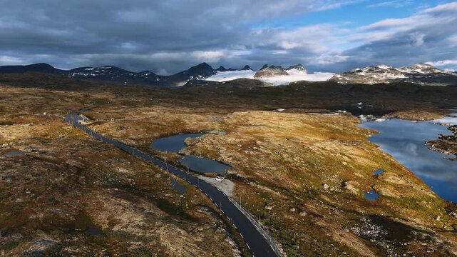 White camper van parked on empty highland road with glacier peaks and tundra lakes, Norway, aerial