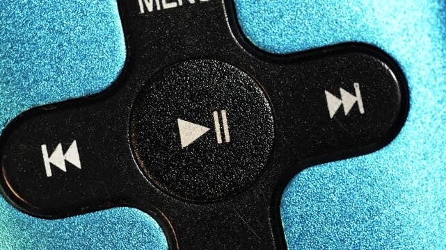 Close up of rotating black cross shaped music player controls with white symbols on metallic blue body