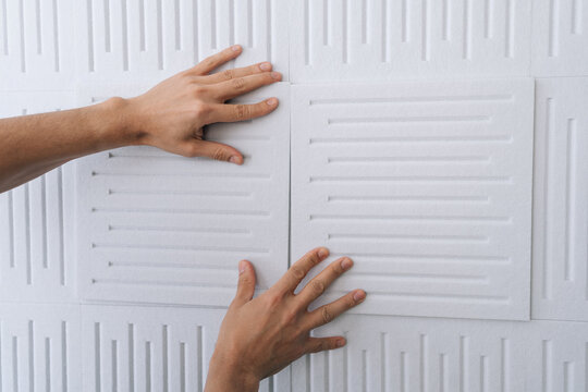 Close-up hand of handyman applying white soundproof acoustic panels onto a wall, improving home interior acoustics and soundproofing a room during renovation or construction