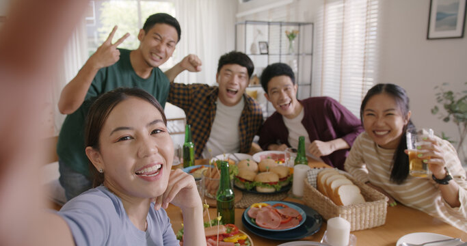 Happy hour diner at home relax smile look at camera shooting video photo on mobile app. Group of asia people young adult friend man and woman sit at dining table joy fun talk or eat food drink beer.