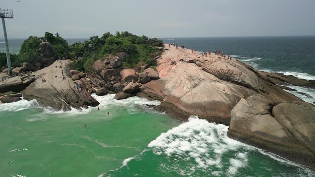 Right aerial orbit over Arpoador Rock during a sunny afternoon with tourists and surfers. Shot at 4K Apple ProRes 422.