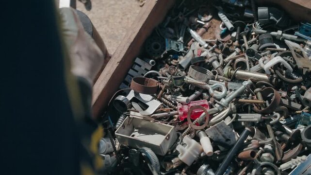 Open wooden box containing assorted metal screws bolts springs and small mechanical parts outdoors