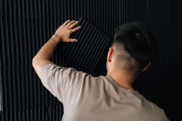 Man installing acoustic foam panels on a wall, enhancing a private studio for soundproofing and...