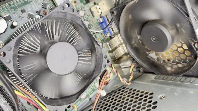 Closeup slow motion shot of twin spinning fans, to cool electrical components and wiring inside the case of a PC desktop computer, which is opened up for testing.
