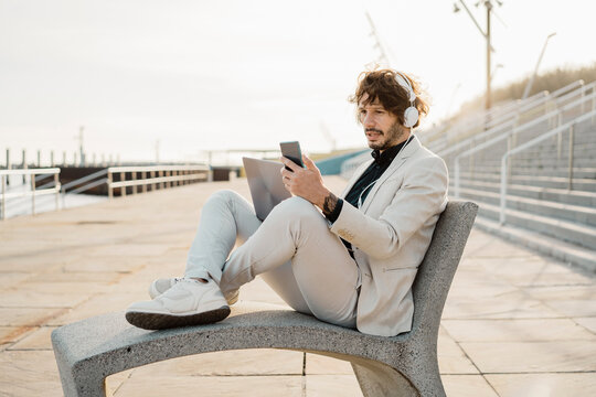 Portrait of shocked businessman with headphones and laptop looking at his mobile phone