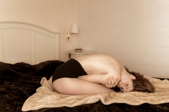 Barechested young woman huddled on the bed at home