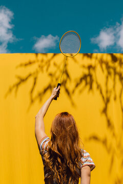 Woman holding badminton racket over yellow wall during sunny day