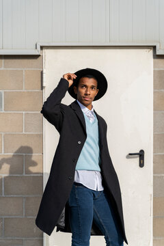 Fashionable young man holding hat while standing against door on sunny day