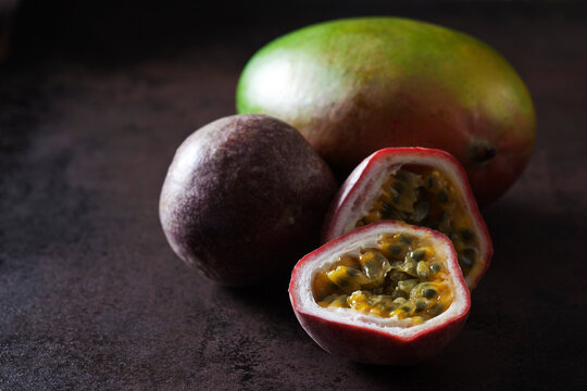 Whole and sliced passion fruit and a mango, on dark ground