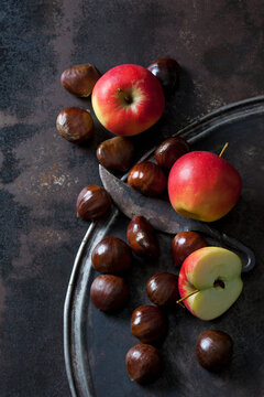 Sliced and whole apples, sweet chestnuts and an old knife on rusty background
