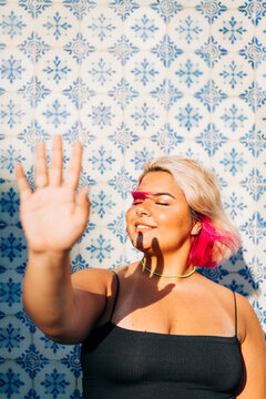 Smiling woman blocking sunlight with hand against wall