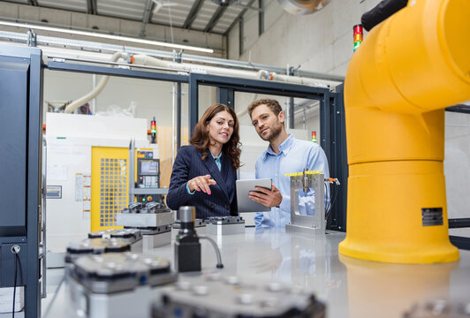 Colleagues in high tech company controlling industrial robots, using digital tablet