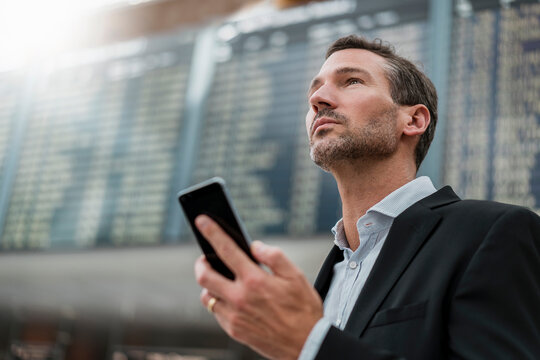 Portrait of businessman with cell phone at arrival departure board at the airport